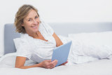 Cheerful blonde woman lying on bed using tablet pc