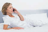 Serious blonde woman lying on bed making a phone call