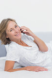 Smiling blonde woman lying on bed making a phone call