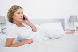 Unsmiling blonde woman lying on bed making a phone call