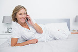 Content blonde woman lying on bed making a phone call