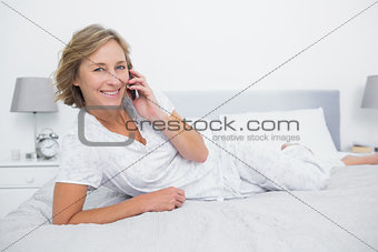 Content blonde woman lying on bed making a phone call