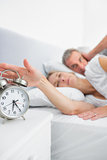 Tired wife turning off alarm clock as husband is covering ears