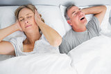 Wife blocking her ears from noise of husband snoring