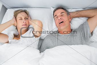 Annoyed wife blocking her ears from noise of husband snoring