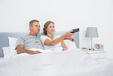 Happy couple watching tv in bed