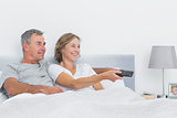 Smiling couple watching tv in bed
