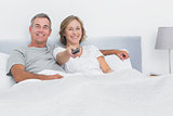 Relaxed couple watching tv in bed looking at camera