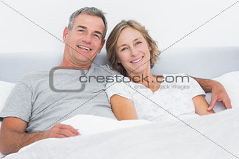 Happy couple cuddling in bed looking at camera