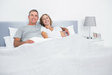 Cheerful couple cuddling in bed looking at camera