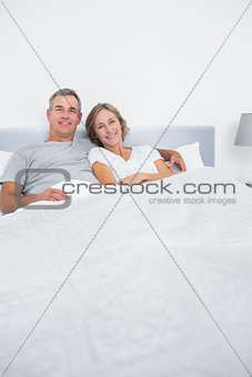 Content couple cuddling in bed looking at camera
