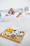 Cuddling couple sleeping with breakfast tray on bed
