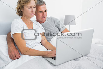 Happy couple using their laptop together in bed