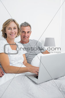 Middle aged couple using their laptop together in bed