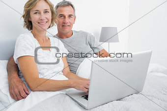 Relaxed couple using their laptop together in bed