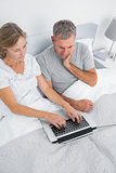 Thoughtful couple using their laptop together in bed