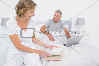 Smiling woman reading book while husband is using laptop