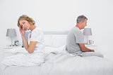 Annoyed couple sitting on different sides of bed having a dispute