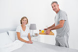 Happy husband bringing breakfast in bed to wife