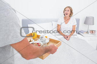 Husband bringing breakfast in bed to surprised wife