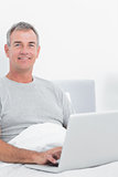 Smiling grey haired man using his laptop in bed