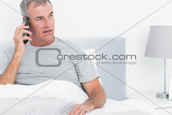 Grey haired man making a phone call in bed