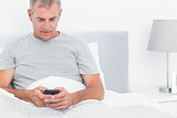 Grey haired man sending a text in bed