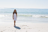 Beautiful brunette in white sun dress walking from the sea