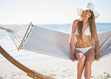 Pretty blonde wearing bikini and sunhat sitting on hammock and smiling
