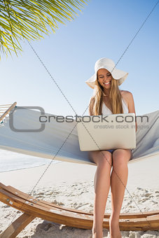 Cheerful blonde sitting on hammock using laptop
