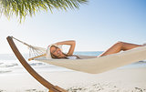 Woman wearing sunhat and bikini relaxing on hammock smiling at camera