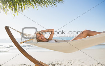 Woman wearing sunhat and bikini relaxing on hammock smiling at camera