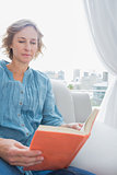 Content blonde woman sitting on her couch reading a book