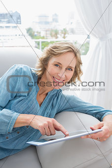 Happy blonde woman relaxing on her couch using her tablet