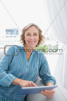 Cheerful blonde woman relaxing on her couch using her tablet