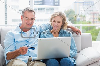 Smiling couple sitting on their couch using the laptop to buy online