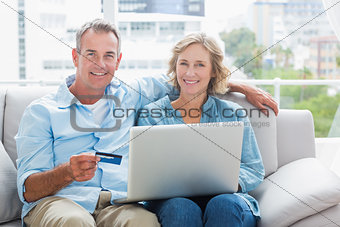 Happy couple sitting on their couch using the laptop to buy online