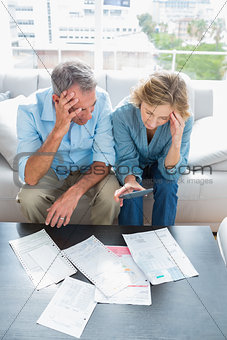 Worried couple sitting on their couch paying their bills
