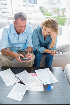 Middle aged couple sitting on their couch paying their bills
