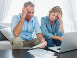 Worried couple paying their bills online with laptop
