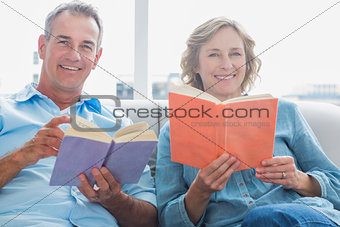 Relaxed couple reading books on the couch smiling at camera