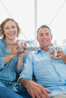 Happy middle aged couple sitting on the couch having coffee