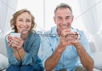 Smiling middle aged couple sitting on the couch having coffee