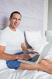 Smiling man using laptop on bed