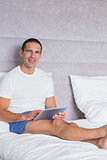 Smiling man using tablet pc on bed