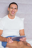Happy man using his tablet pc sitting on bed