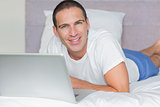 Happy man lying on bed using his laptop