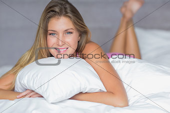 Pretty blonde lying on her bed hugging pillow smiling