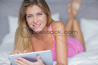 Smiling blonde lying on her bed using her tablet pc