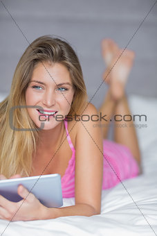 Thoughtful blonde lying on her bed using her tablet pc